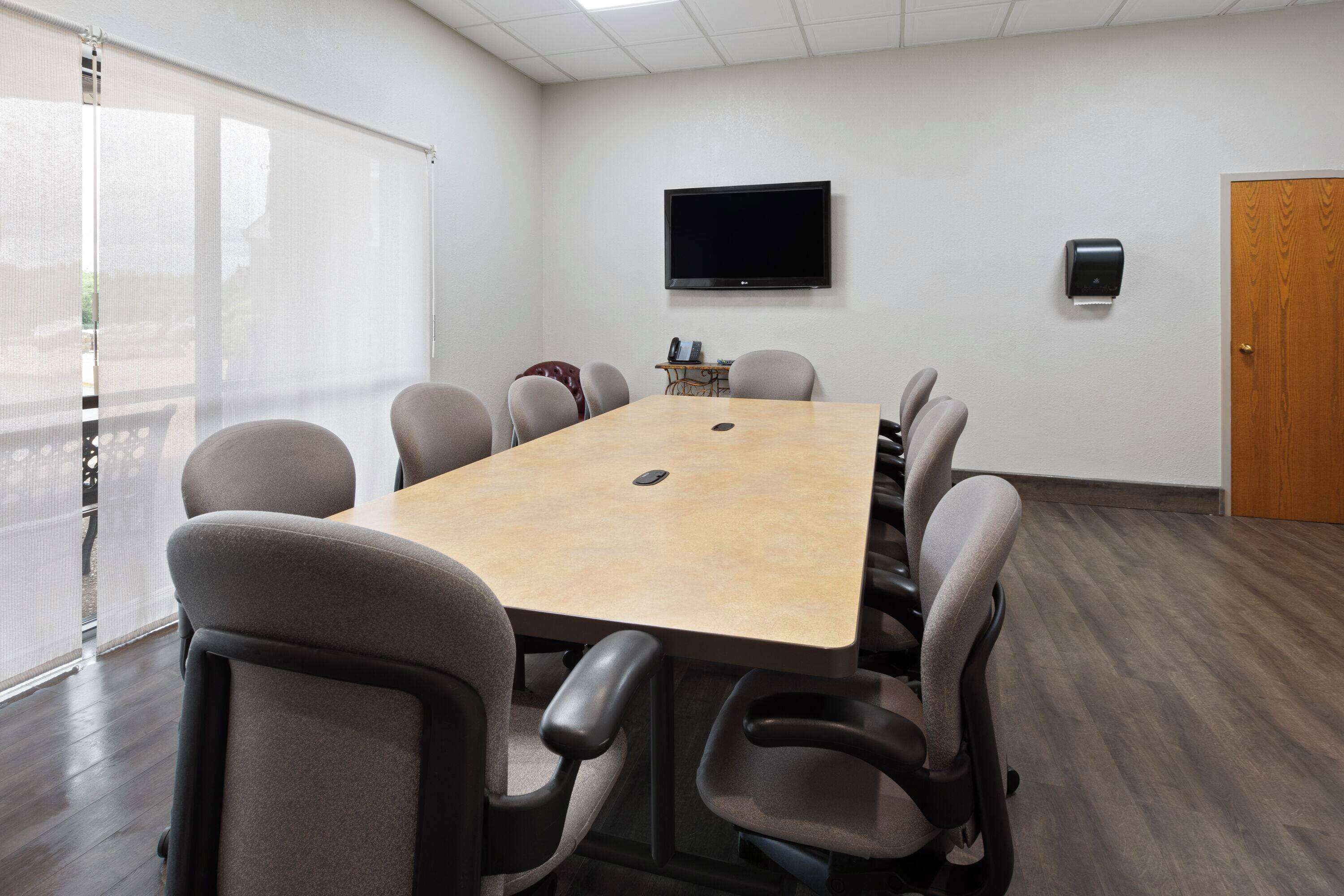 A conference room with a large table, six chairs, a TV mounted on the wall, and a door.