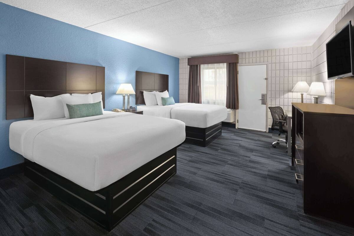 Een hotelkamer met twee bedden, een bureau, een stoel, een televisie en een raam met gordijnen.