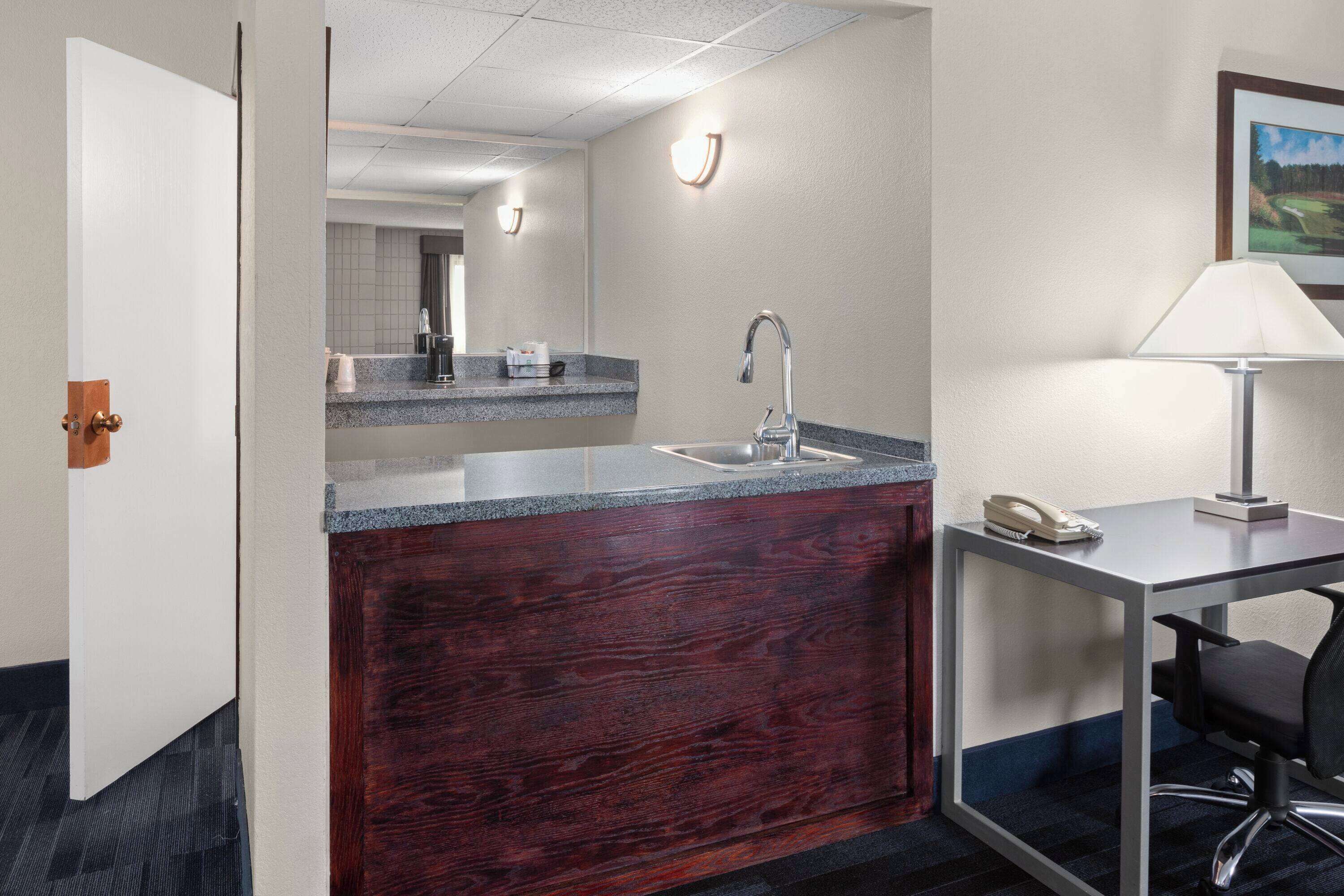 Habitación de hotel con tocador de madera, lavamanos, espejo, escritorio con silla y lámpara.