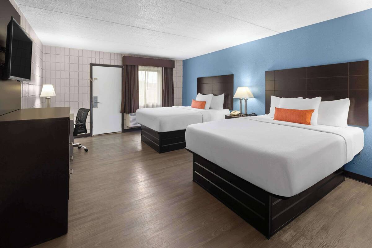 Een hotelkamer met twee bedden, een bureau, een stoel, een televisie en een deur.