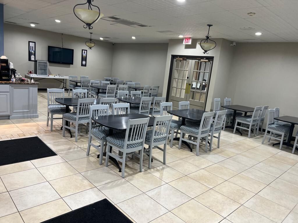 Un espace repas comprenant plusieurs tables et chaises, un comptoir de cuisine et un téléviseur fixé au mur.