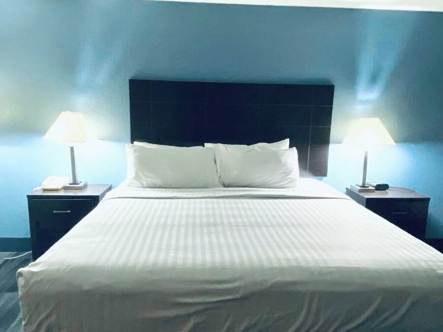 A neatly made bed with white linens, two bedside tables with lamps, and a dark headboard.