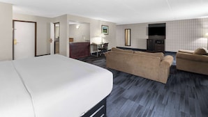 A hotel room with a large bed, two sofas, a desk with a lamp, a microwave, and a TV.