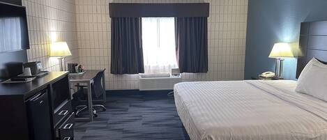 A hotel room with a bed, desk, chair, TV, lamps, and a window with curtains.