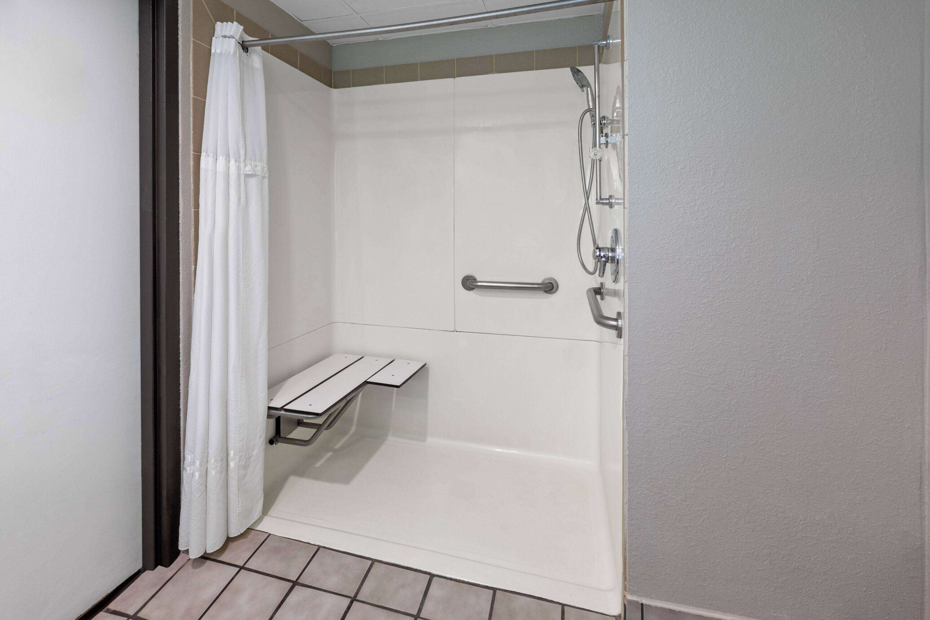 A shower area with a white curtain, a handheld showerhead, and a grab bar.