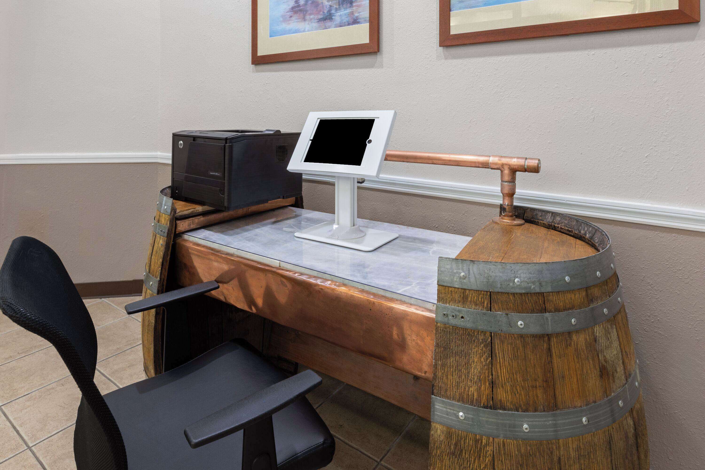 Una mesa de recepción con un monitor de computadora, una impresora y un barril de madera.