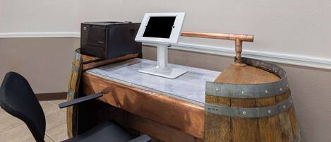 Una mesa de recepción con un monitor de computadora, una impresora y un barril de madera.