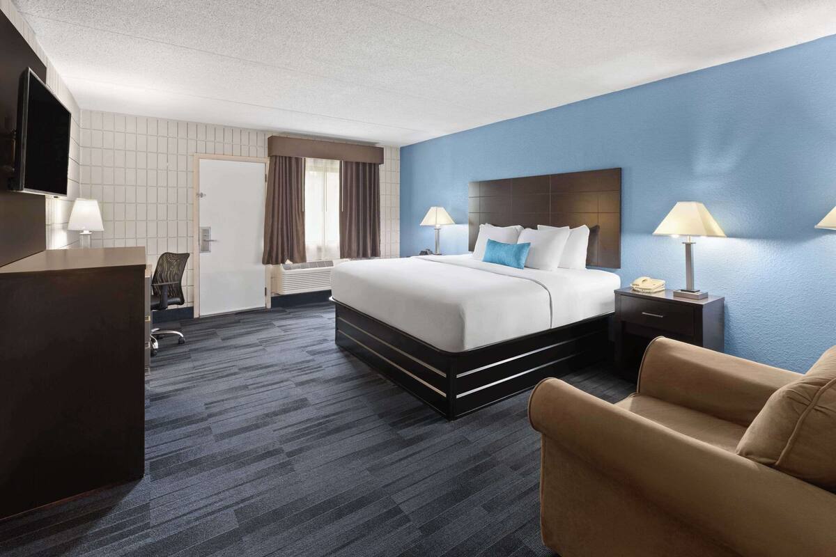 Een hotelkamer met een groot bed, een bureau met stoel, een televisie en een lamp.