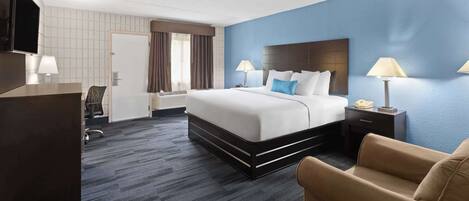 Una habitación de hotel con una cama grande, un escritorio con silla, un televisor y una lámpara.