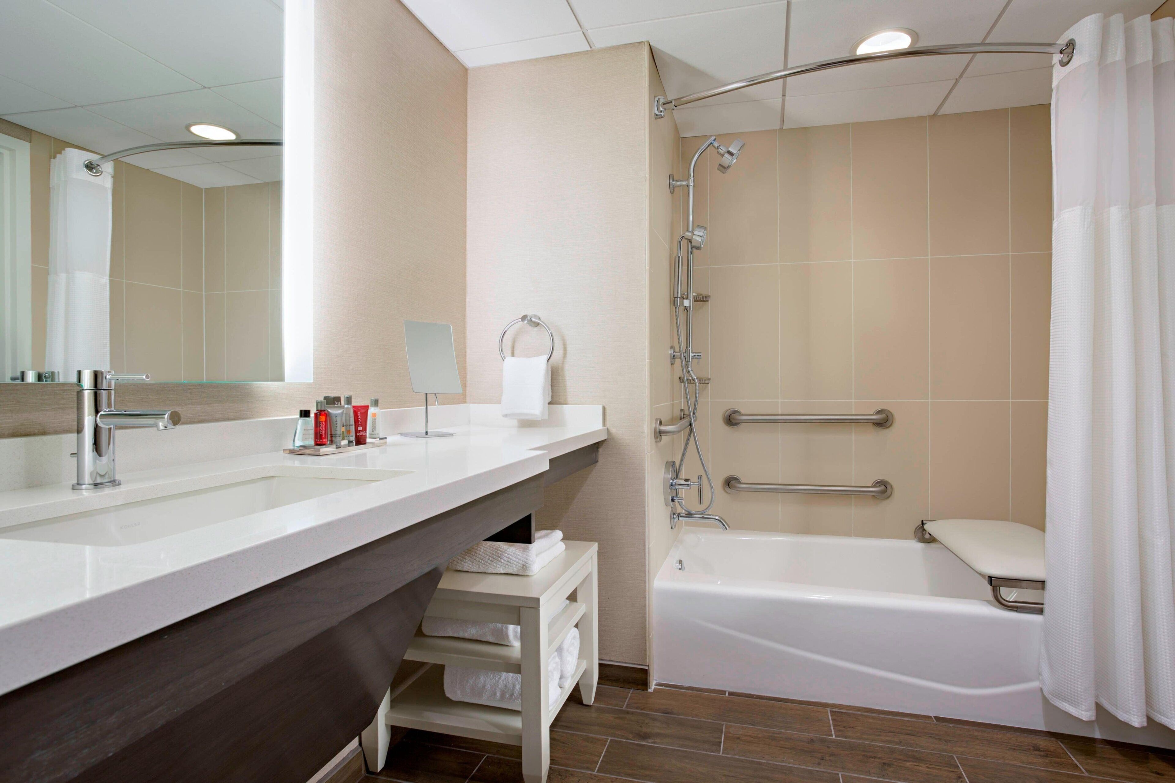 Une salle de bain moderne dotée d’un meuble-lavabo à deux vasques, d’une baignoire et d’une douche équipée de barres d’appui.