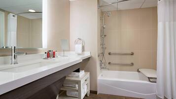 Une salle de bain moderne dotée d’un meuble-lavabo à deux vasques, d’une baignoire et d’une douche équipée de barres d’appui.