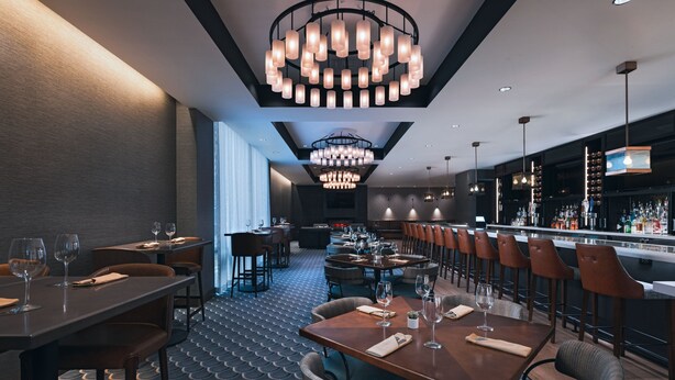 A modern restaurant with a bar area, featuring a patterned floor, multiple dining tables, and contemporary lighting fixtures. - Houston Marriott Medical Center/Museum District (Houston)