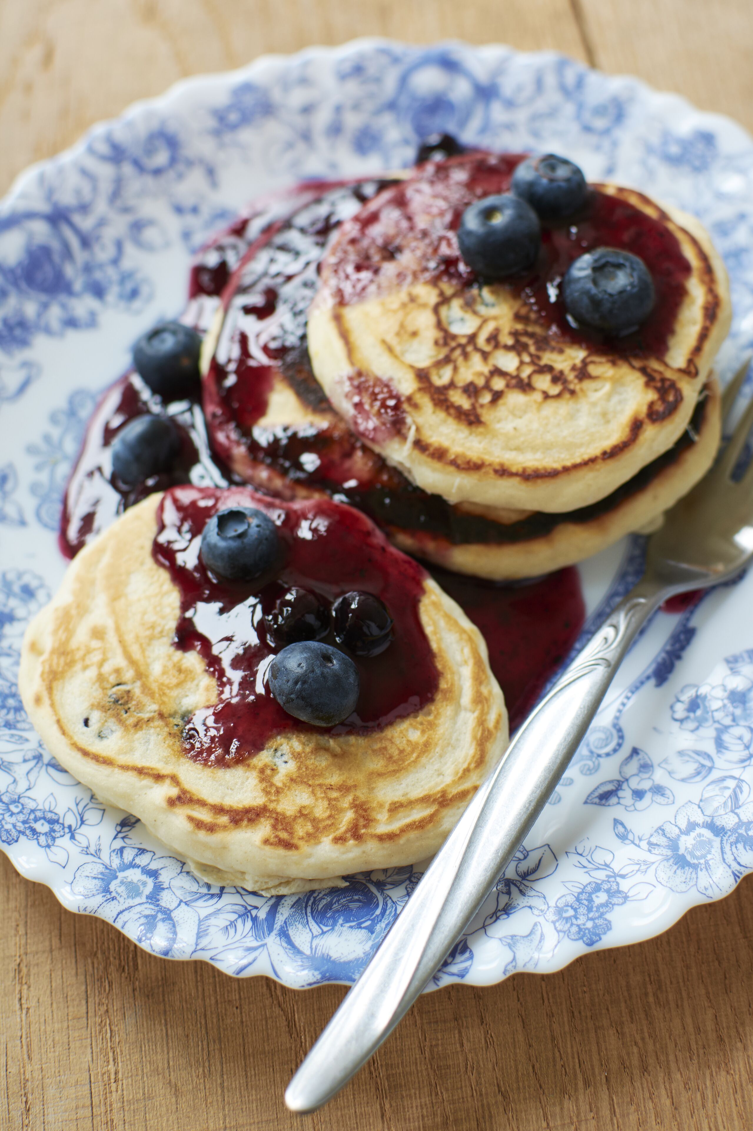A plate of pancakes with blueberries and syrup, served on a floral-patterned plate.