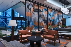 A modern lounge area with a sofa, chairs, and a round table. A decorative wall with vertical elements is visible.