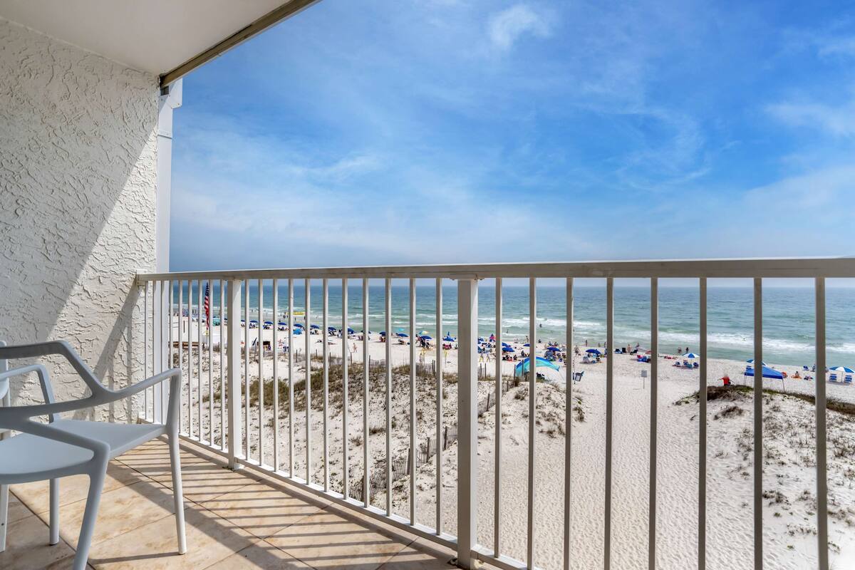 A balcony with a view of a beach, featuring a white railing and a single white chair.