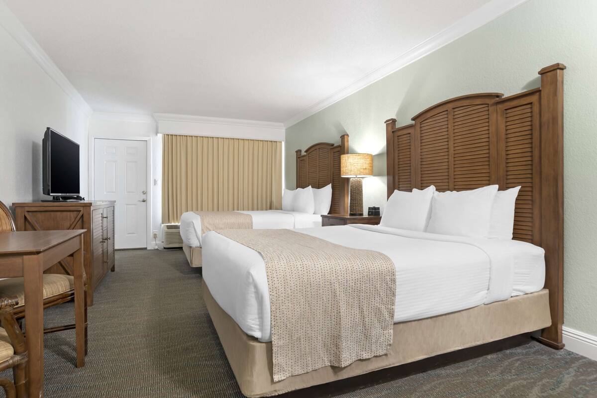 A hotel room with a large bed, a smaller bed, a desk with a TV, and a lamp.