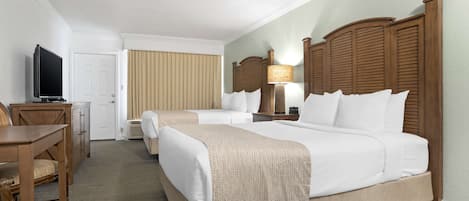 A hotel room with a large bed, a smaller bed, a desk with a TV, and a lamp.