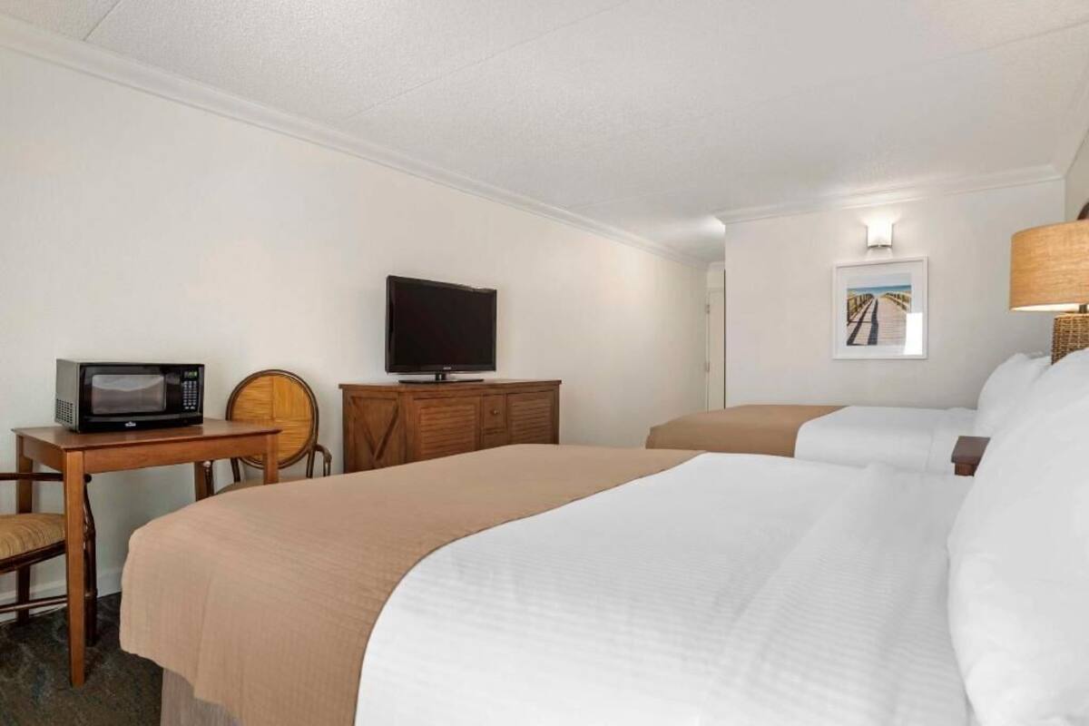 A hotel room with two beds, a television on a wooden dresser, a microwave, a chair, and a lamp.