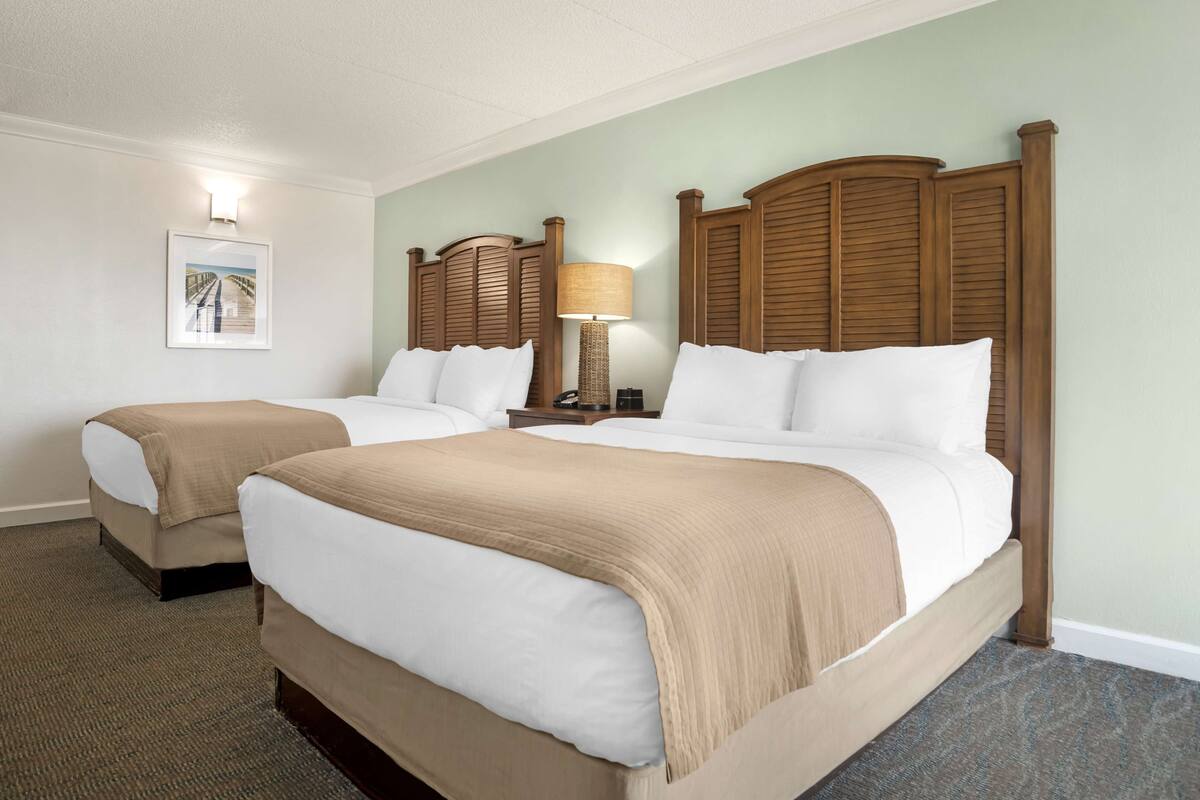 A hotel room with two beds, a lamp, a framed picture on the wall, and a carpeted floor.