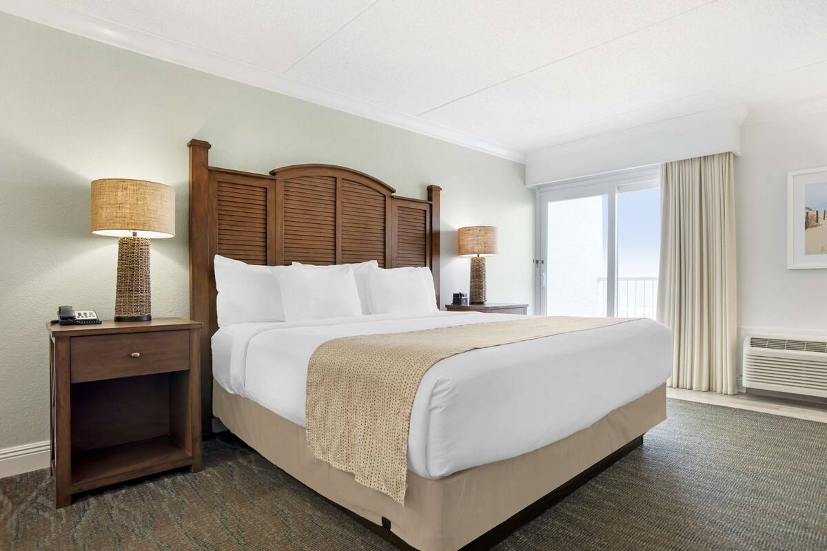 A hotel room with a large bed, two bedside lamps, a nightstand, and a window with curtains.