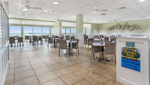 A spacious indoor dining area with multiple tables and chairs, a sign indicating a requirement for swimwear, and a view through large windows. - Best Western On The Beach (Gulf Shores)