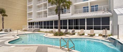 A swimming pool with a palm tree, lounge chairs, and a multi-story building with balconies.