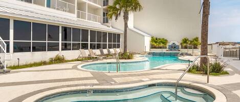 A hotel with a pool area featuring multiple swimming pools, lounge chairs, and palm trees.