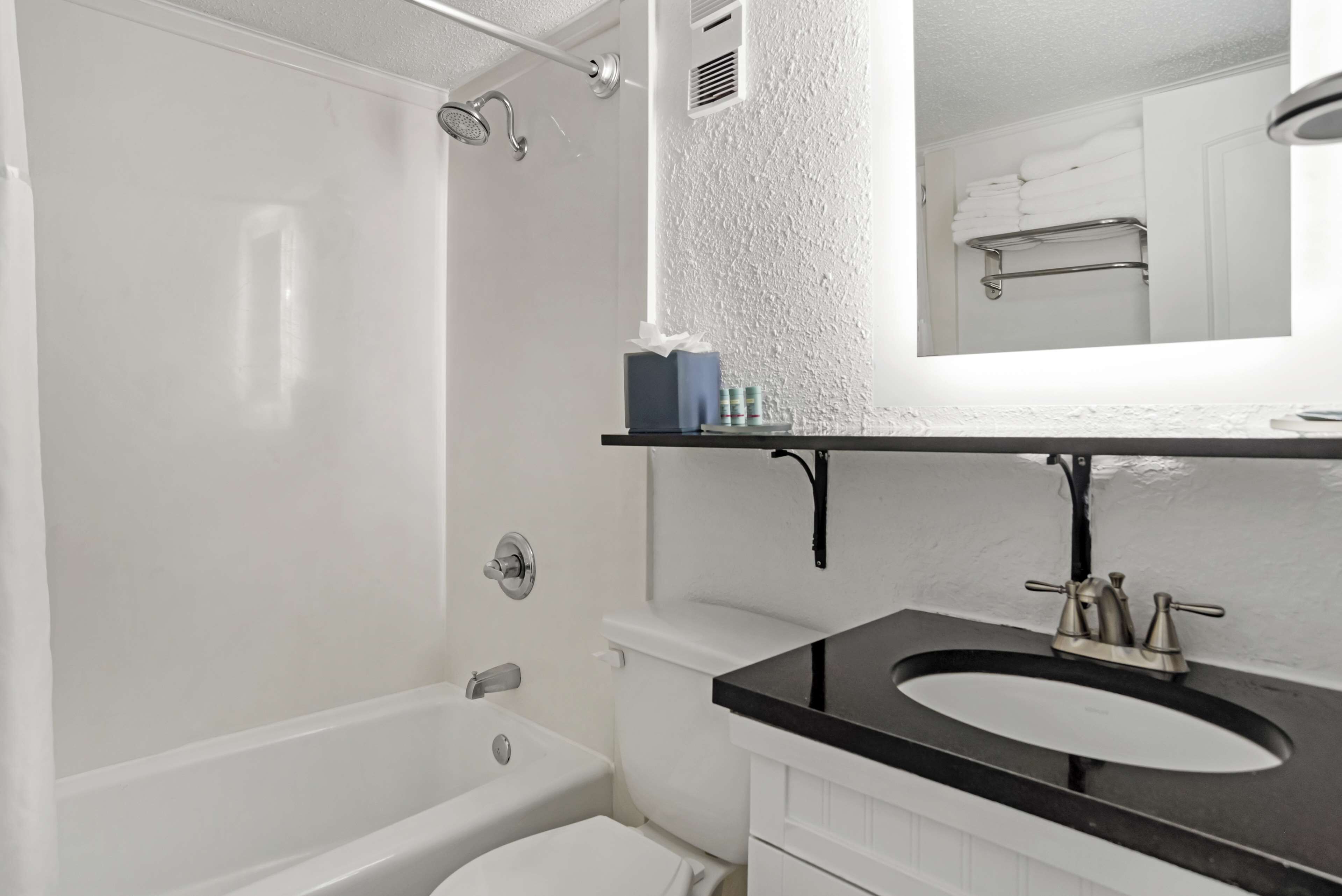 Un baño con una bañera blanca, un lavabo negro y un espejo sobre el lavabo.