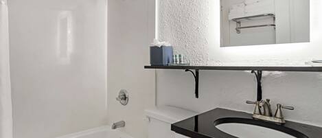 Un baño con una bañera blanca, un lavabo negro y un espejo sobre el lavabo.
