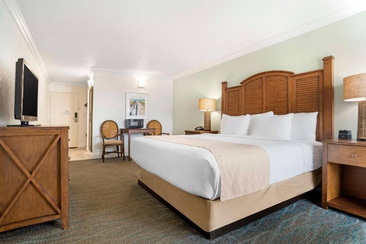 A hotel room with a large bed, a desk, a chair, a television, and a lamp.