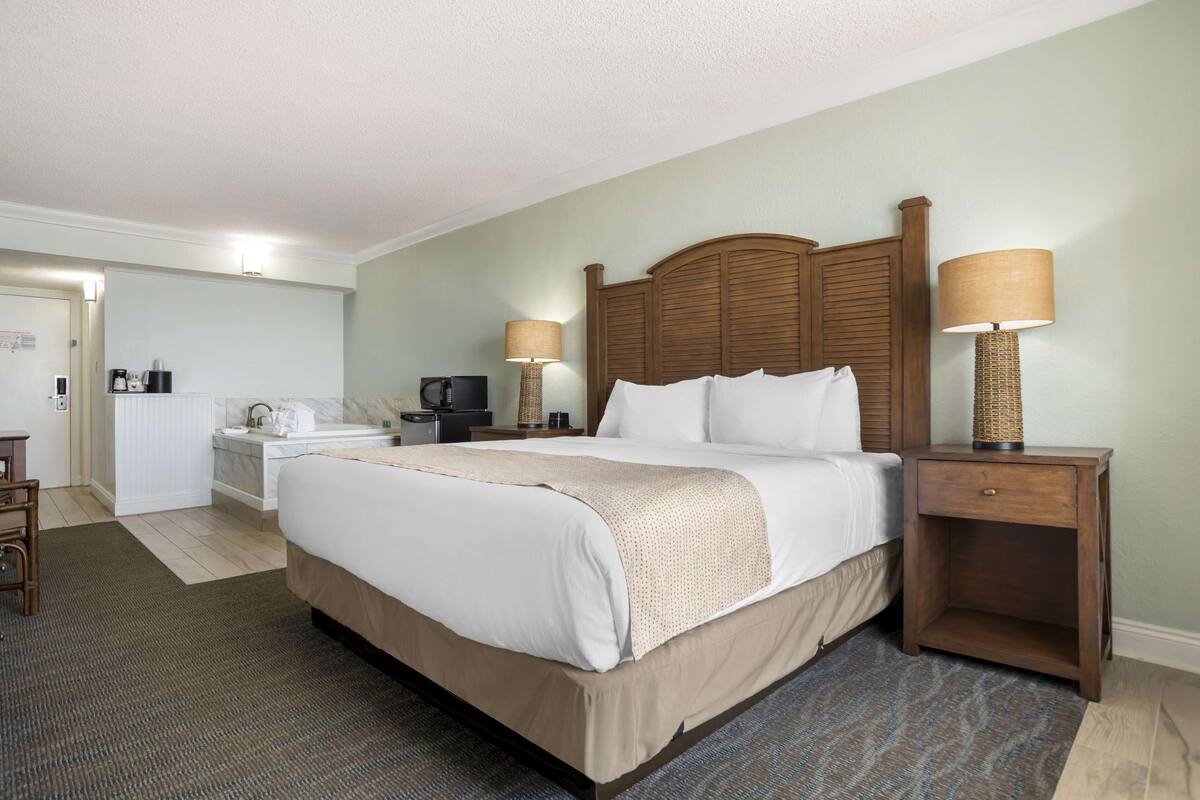 A hotel room with a large bed, two bedside tables with lamps, a desk with a chair, a coffee maker, and a television.