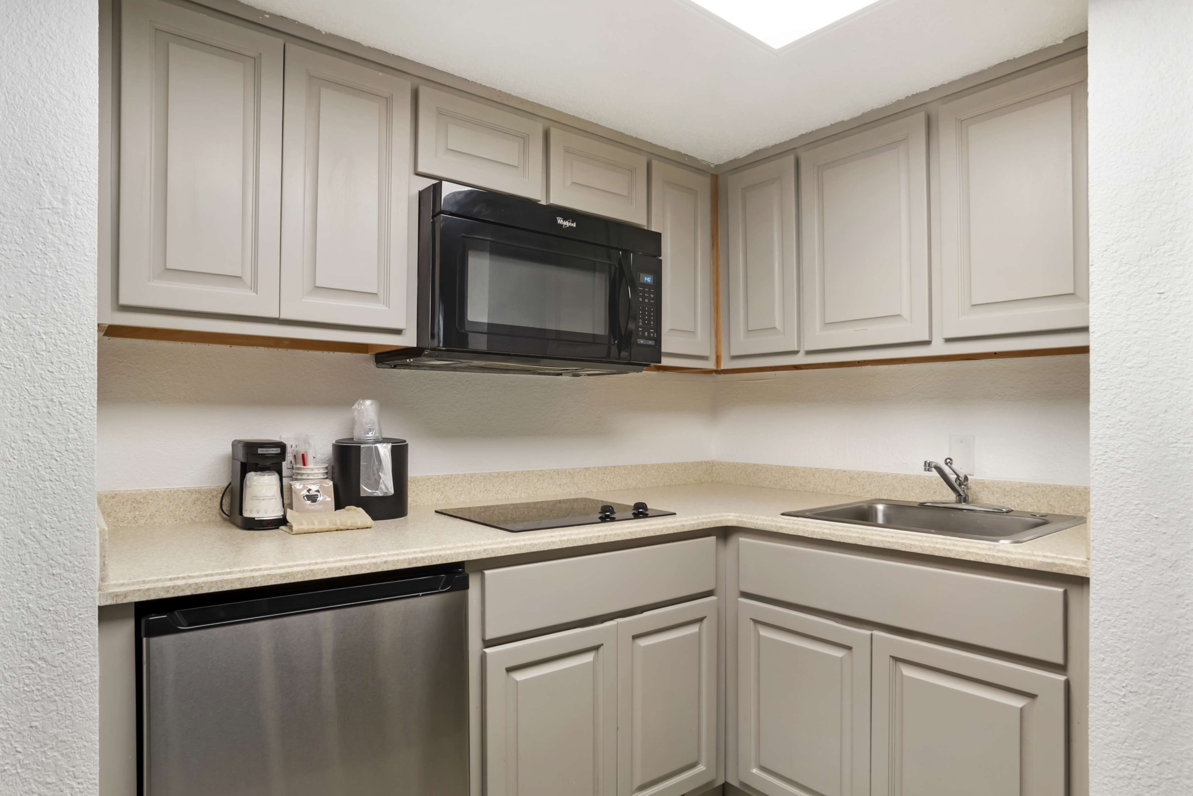Una cocina compacta con armarios blancos, microondas integrado, cafetera y lavavajillas.