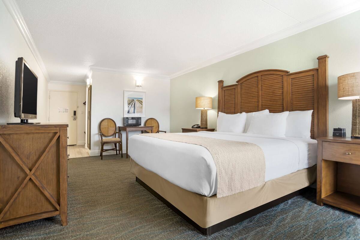 A hotel room with a large bed, a desk, a chair, a television, and a lamp.