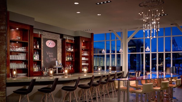 A bar area with a long counter, stools, and a view of the outside at dusk.