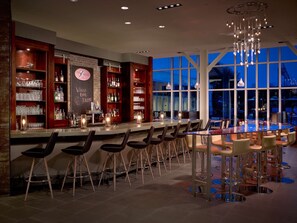 Un espace bar doté d’un long comptoir, de tabourets et offrant une vue sur l’extérieur au crépuscule.