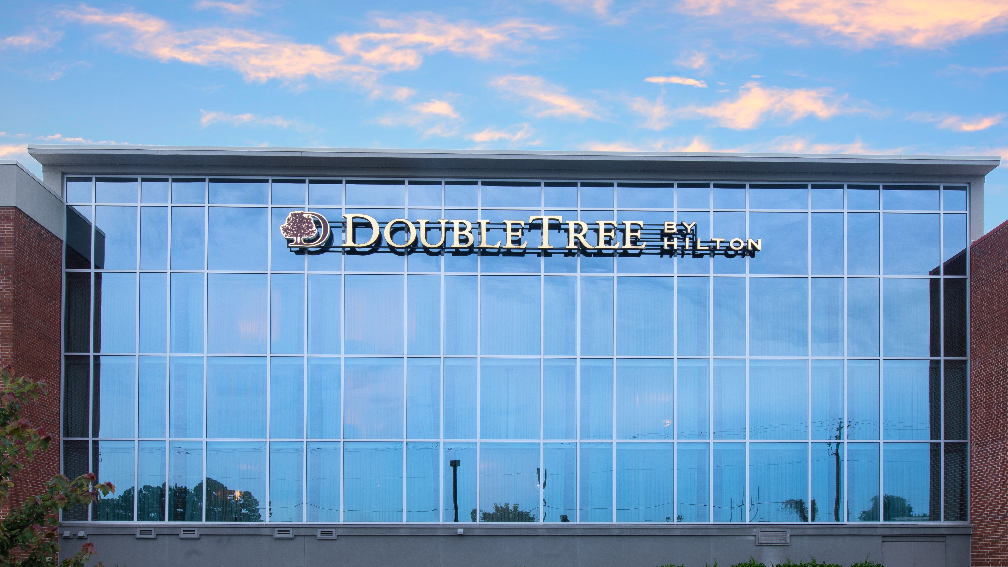 Fachada de un hotel DoubleTree by Hilton con un amplio ventanal que refleja el cielo y los edificios circundantes.