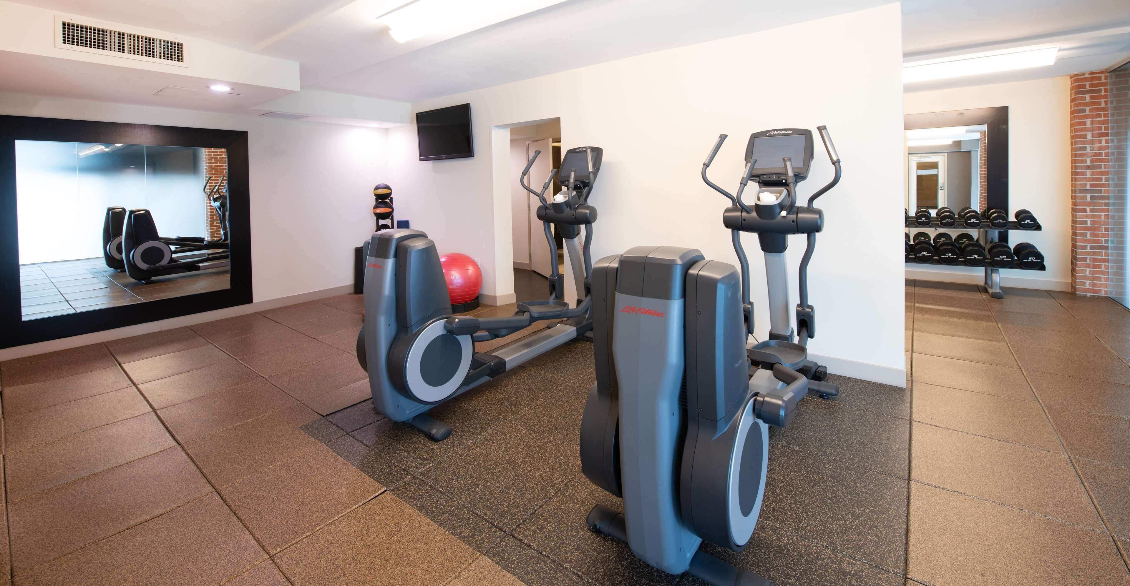 Un gimnasio con cintas de correr, elípticas y una pelota de ejercicios roja.