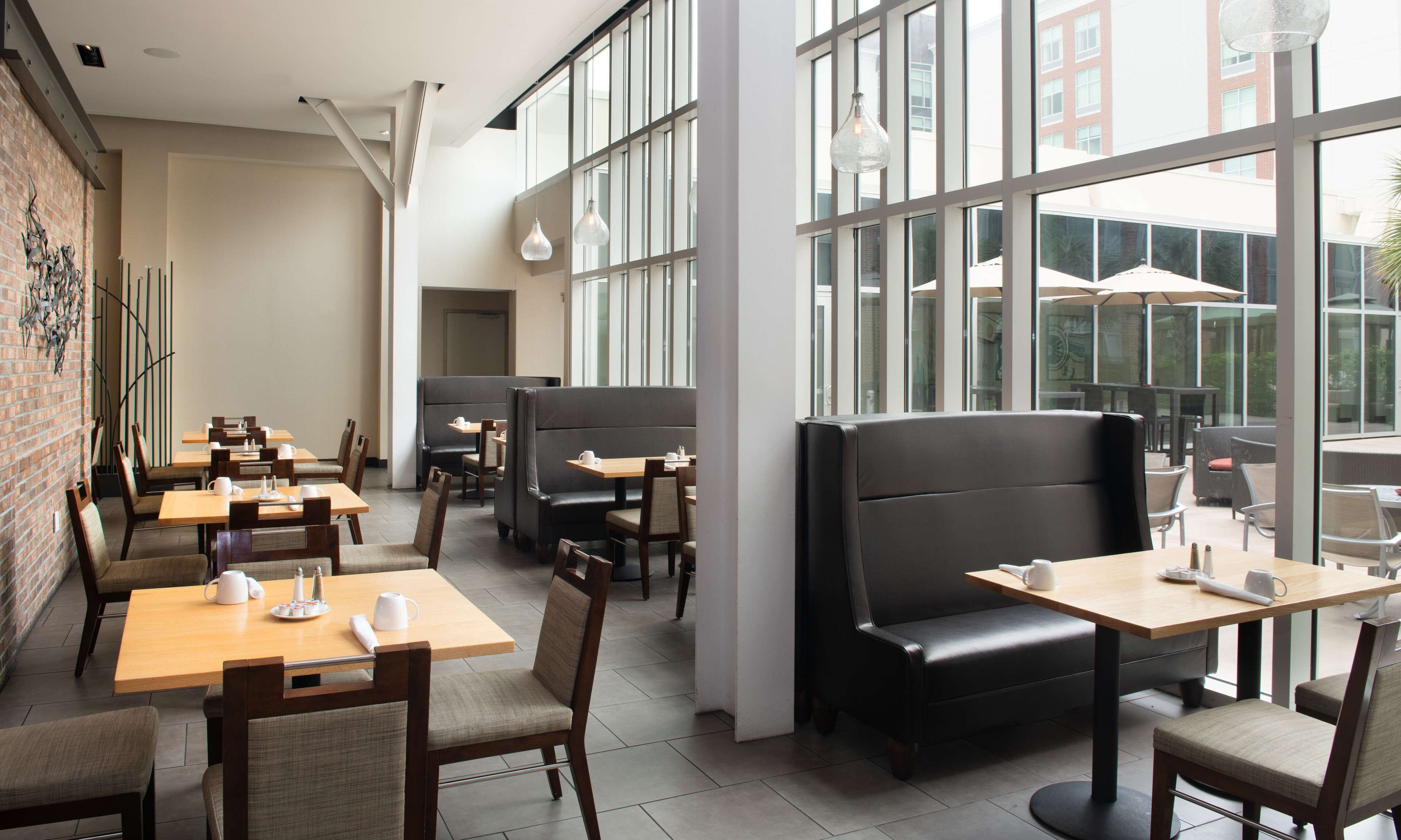 A modern cafe with multiple seating areas, including tables and booths, and large windows offering views of the outside.
