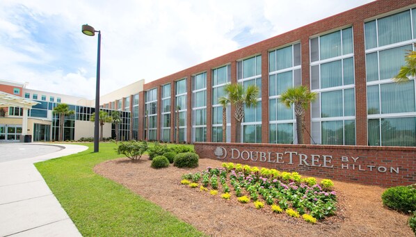 Un hotel DoubleTree by Hilton con fachada de ladrillo, ventanas grandes y un jardín ajardinado con diversas plantas y flores.