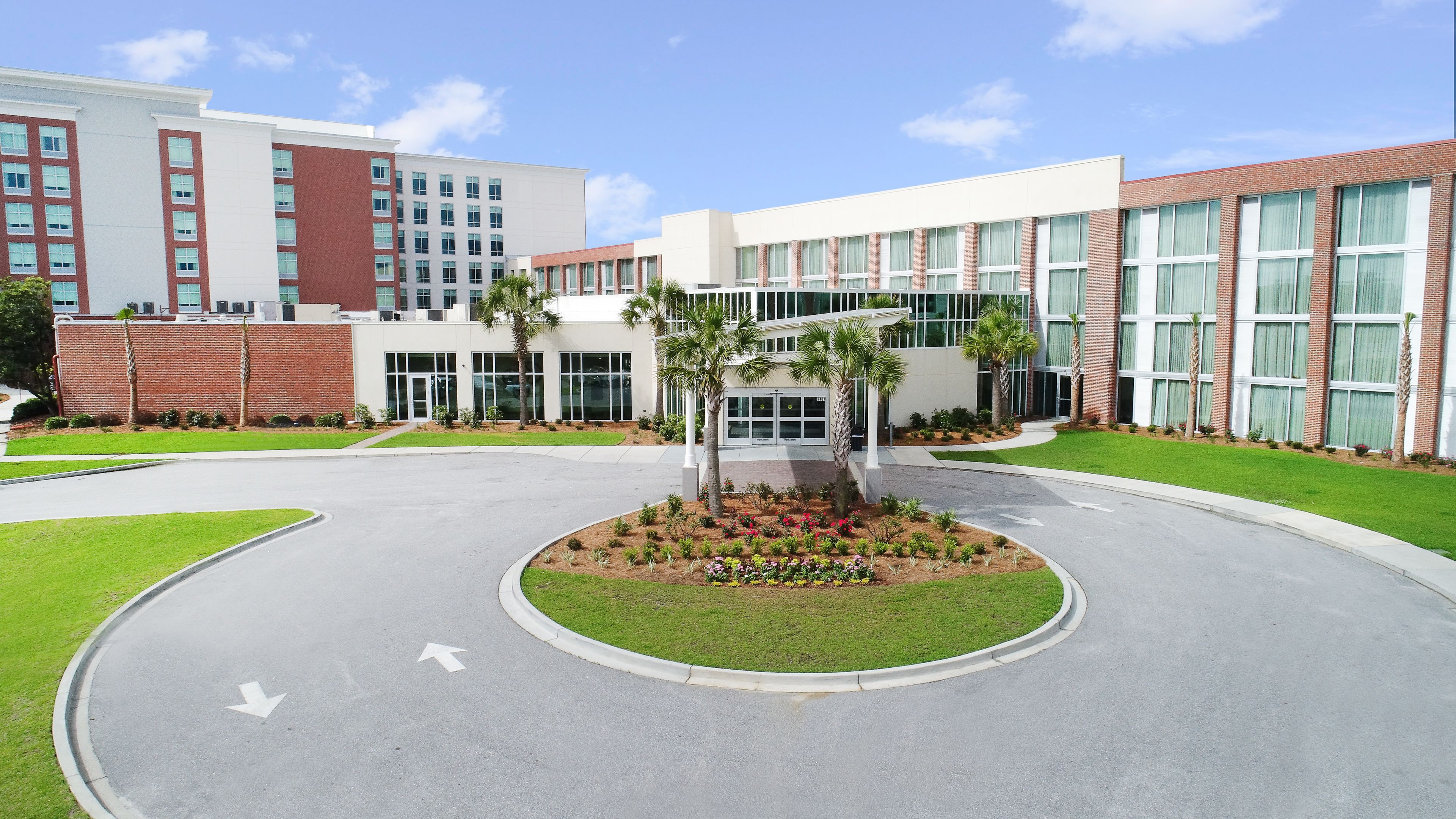 A modern building with a central courtyard, palm trees, and a well-maintained lawn.