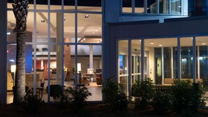 A modern building with large windows, a palm tree, and indoor seating areas.
