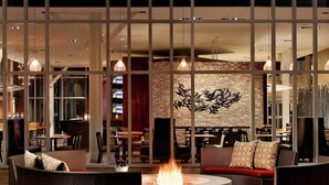 A modern lounge area with wicker furniture, a central fire pit, and a brick wall with a decorative metal sculpture.