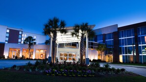 A modern hotel with a central entrance, palm trees, and a well-maintained garden.