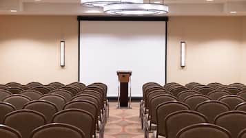 A conference room with rows of chairs, a podium, and a large screen at the front.