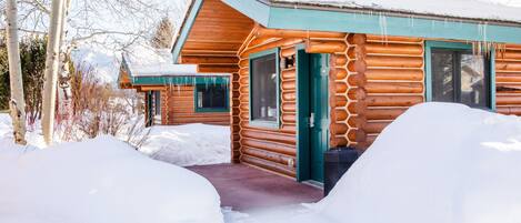 A log cabin with a green door and windows, surrounded by snow.