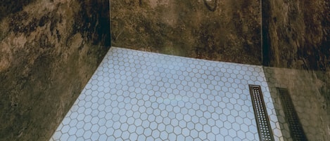 A shower with a hexagonal tile floor, a handheld showerhead, and a wall-mounted faucet.