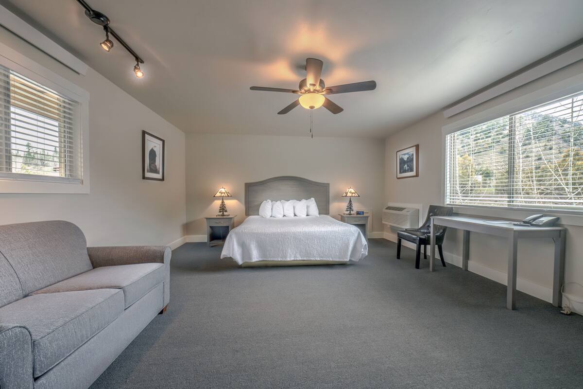 A bedroom with a bed, a desk, a chair, a sofa, and a ceiling fan.