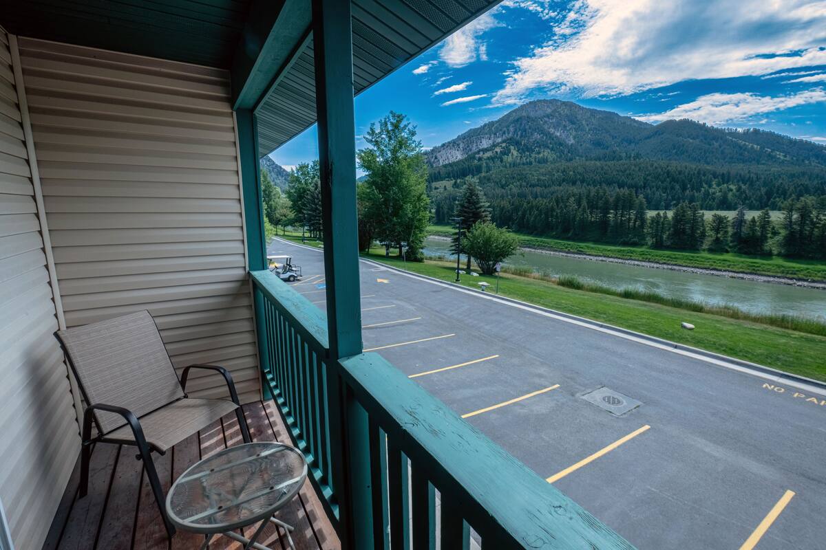 A porch with a view of a parking lot, a river, and mountains.
