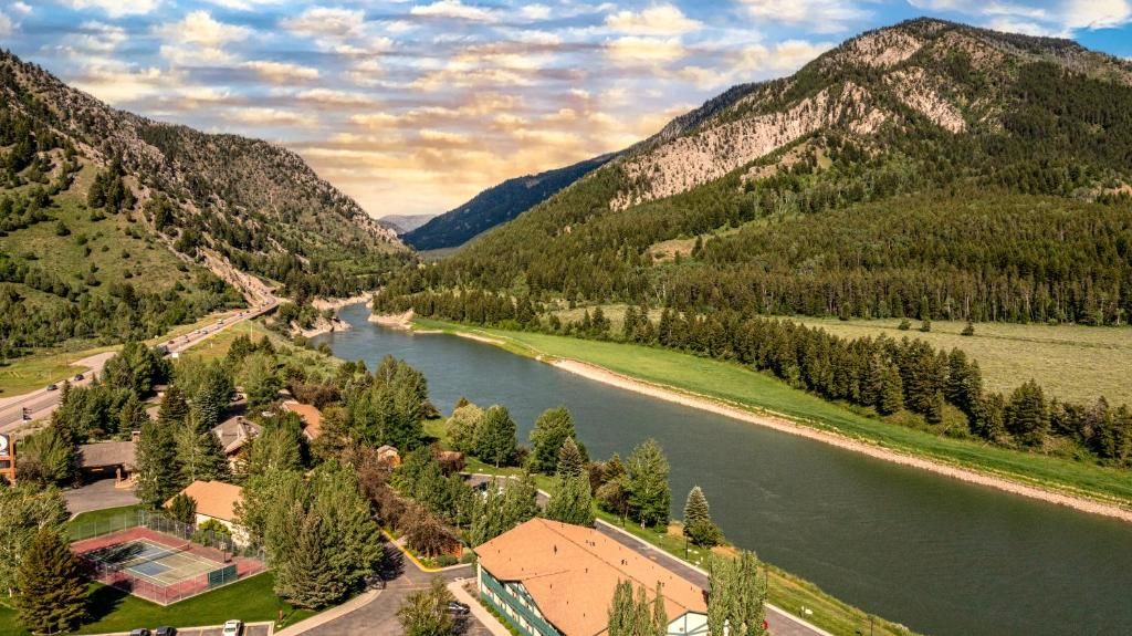 Une rivière qui traverse une vallée, avec des montagnes de chaque côté, et qui est bordée de verdure et de quelques bâtiments.