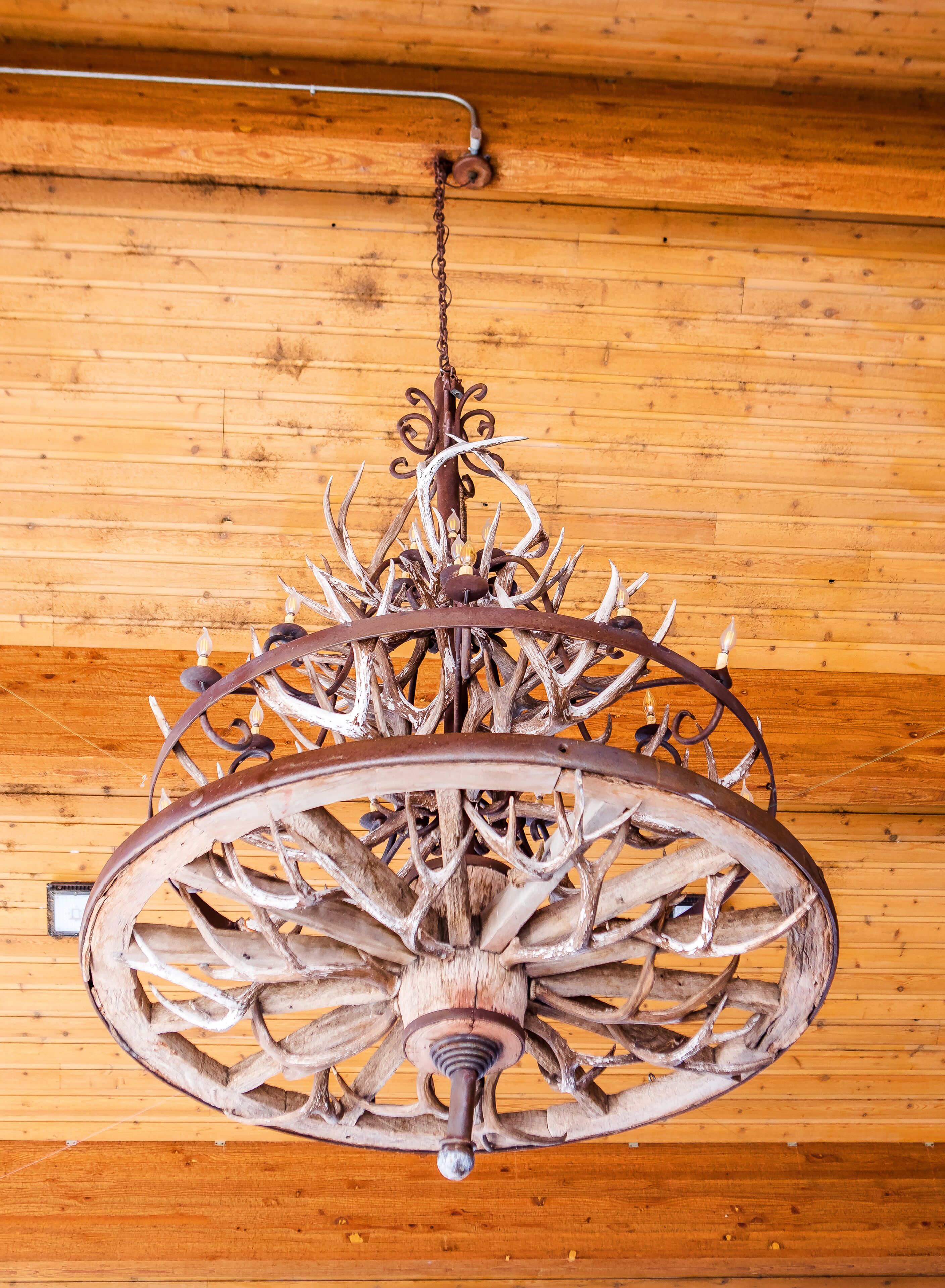 A chandelier with a rustic design, featuring antlers and metalwork, hanging from a wooden ceiling.
